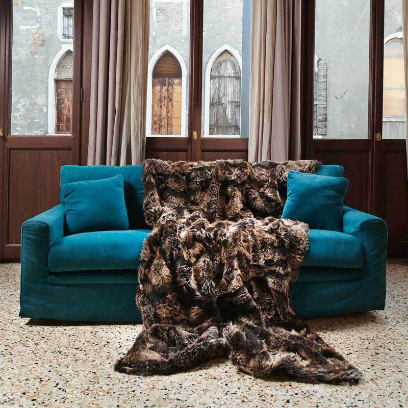 Luxurious full size truffle brown sheep skin fur blanket spread out on a teal blue sofa with glass windows in the background
